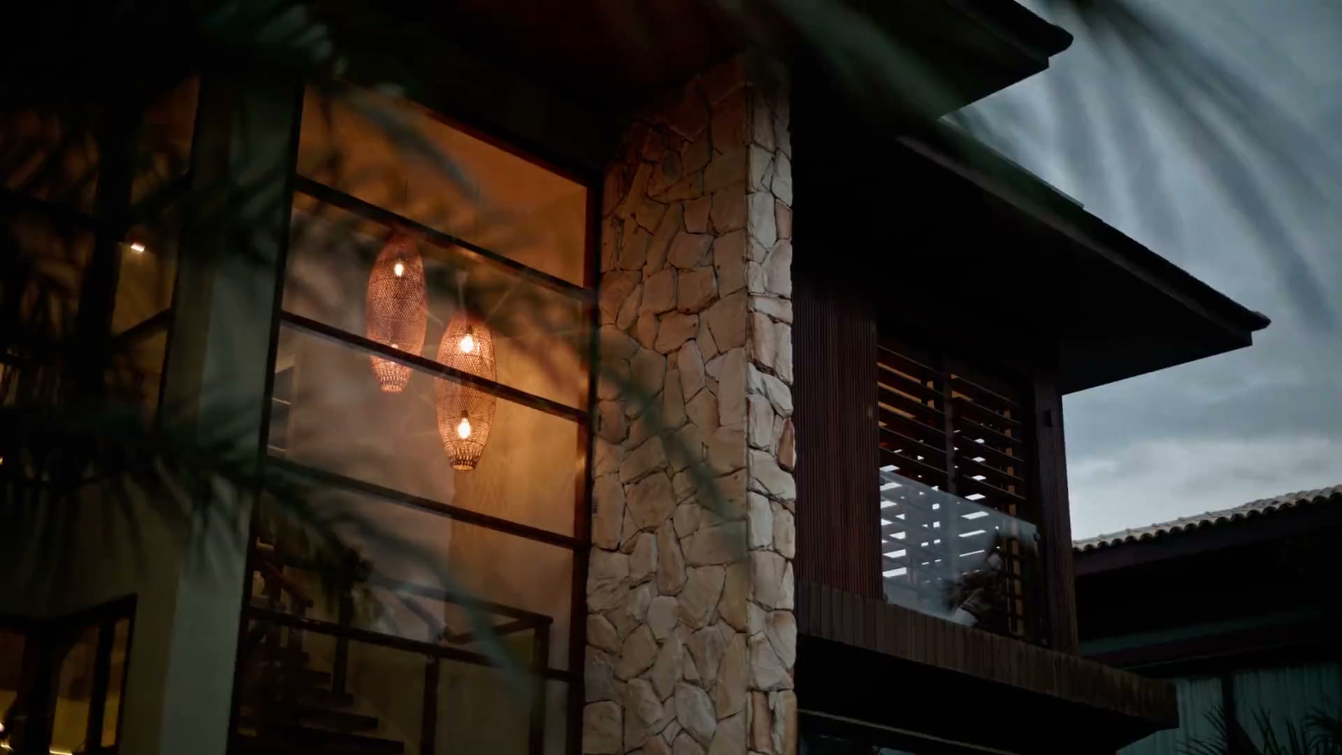 A home at dusk, warm light behind floor-to-ceiling glass